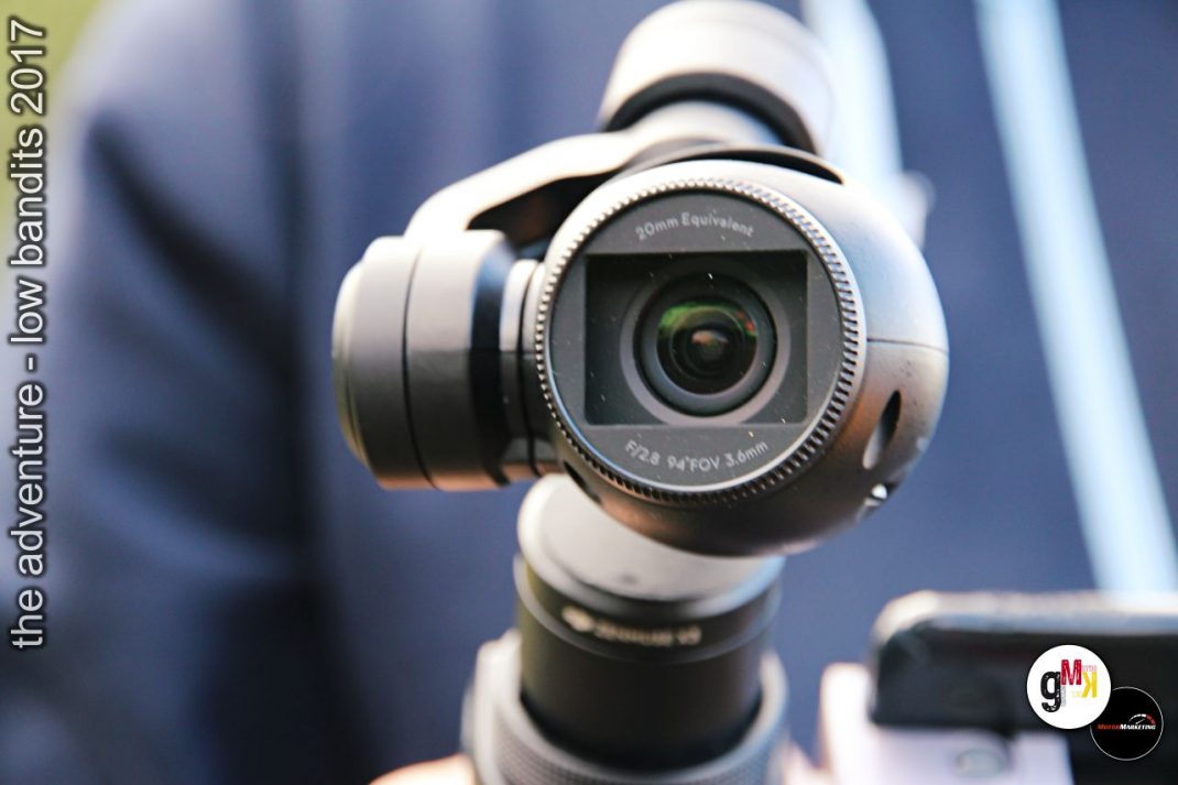 Stabilisierte Kameradrohne mit Gimbal wird von Hand gehalten, im Hintergrund verschwommene Fahrzeugsilhouette