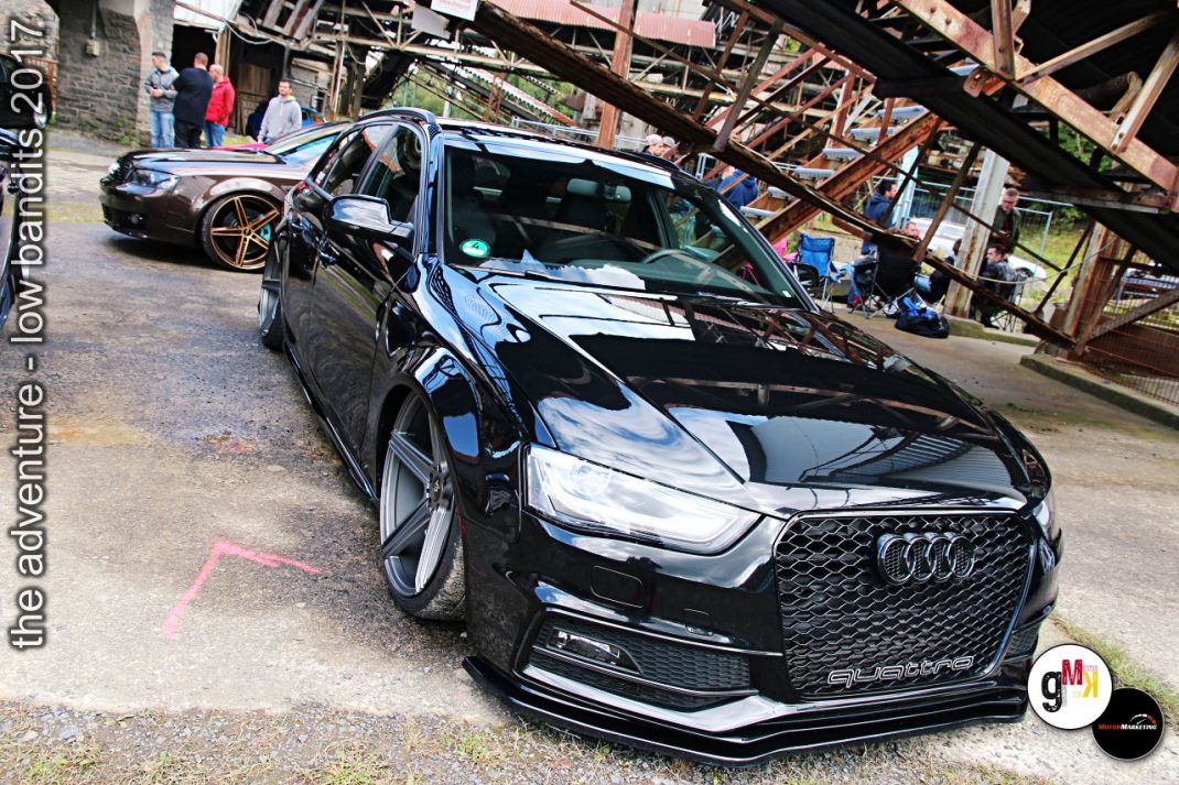 Schwarzer Audi-Sportwagen mit tiefer Tuning-Auslegung auf Steinbruch-Gelände, weitere Youngtimer dahinter, Besucher im Hintergrund