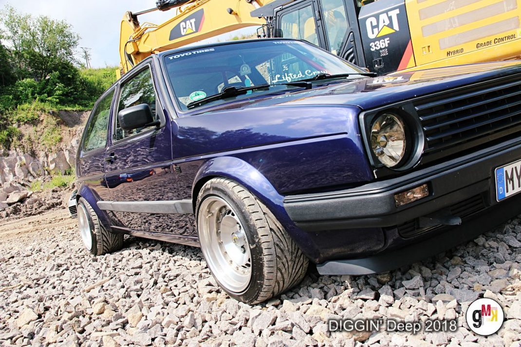 Blauer Youngtimer-Golf auf Kiesgelände vor gelber Baumaschine bei der DIGGIN' Deep 2018 in der Eifel