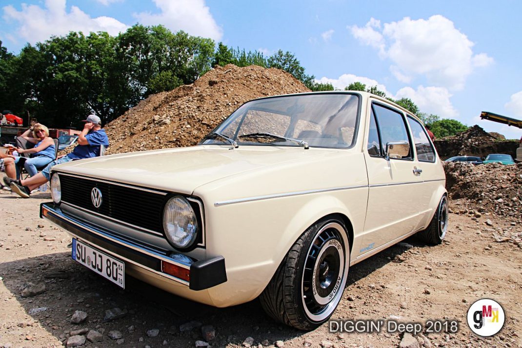 VW Golf Oldtimer in Creme-Weiß bei der Youngtimer-Tour DIGGIN' Deep 2018 in der Eifel, im Hintergrund Zuschauer und Erdaufschüttungen