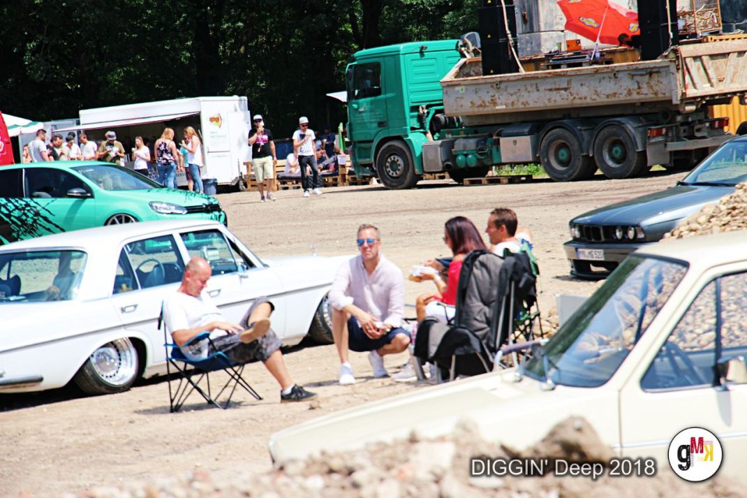 Teilnehmer sitzen zwischen Oldtimern und Youngtimern auf dem Veranstaltungsgelände von DIGGIN' Deep in der Eifel, im Hintergrund Lastwagen und Besucher
