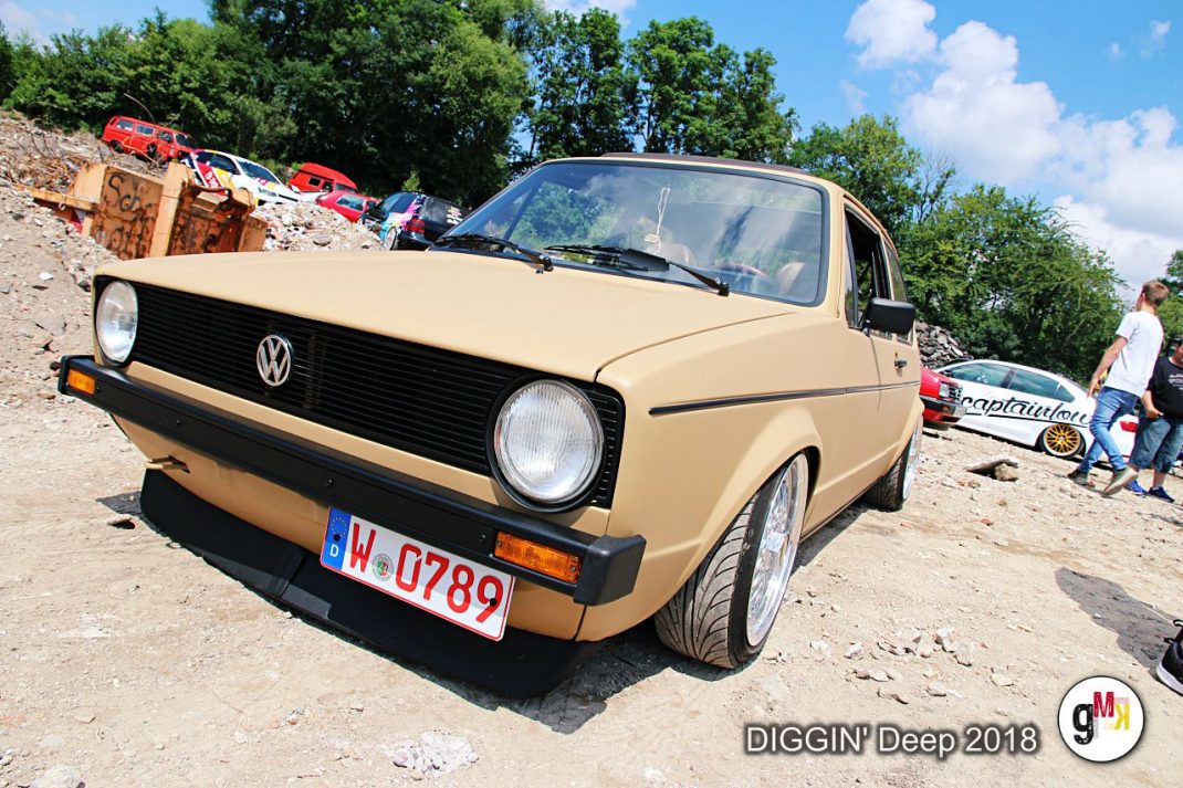 Beige Volkswagen Golf auf Kiesplatz, im Hintergrund rote Oldtimer und Teilnehmer der DIGGIN' Deep 2018 in der Eifel