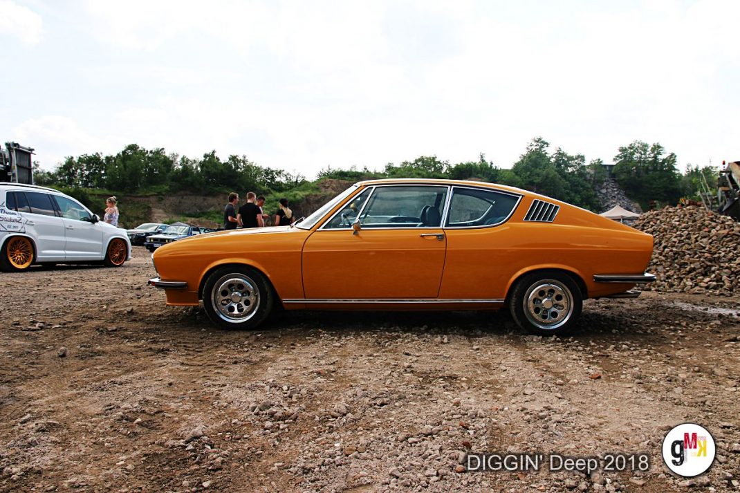 Orangefarbener Oldtimer-Coupé in Seitenansicht auf Kiesgelände, Teilnehmer im Hintergrund bei der Youngtimer-Tour DIGGIN' Deep 2018