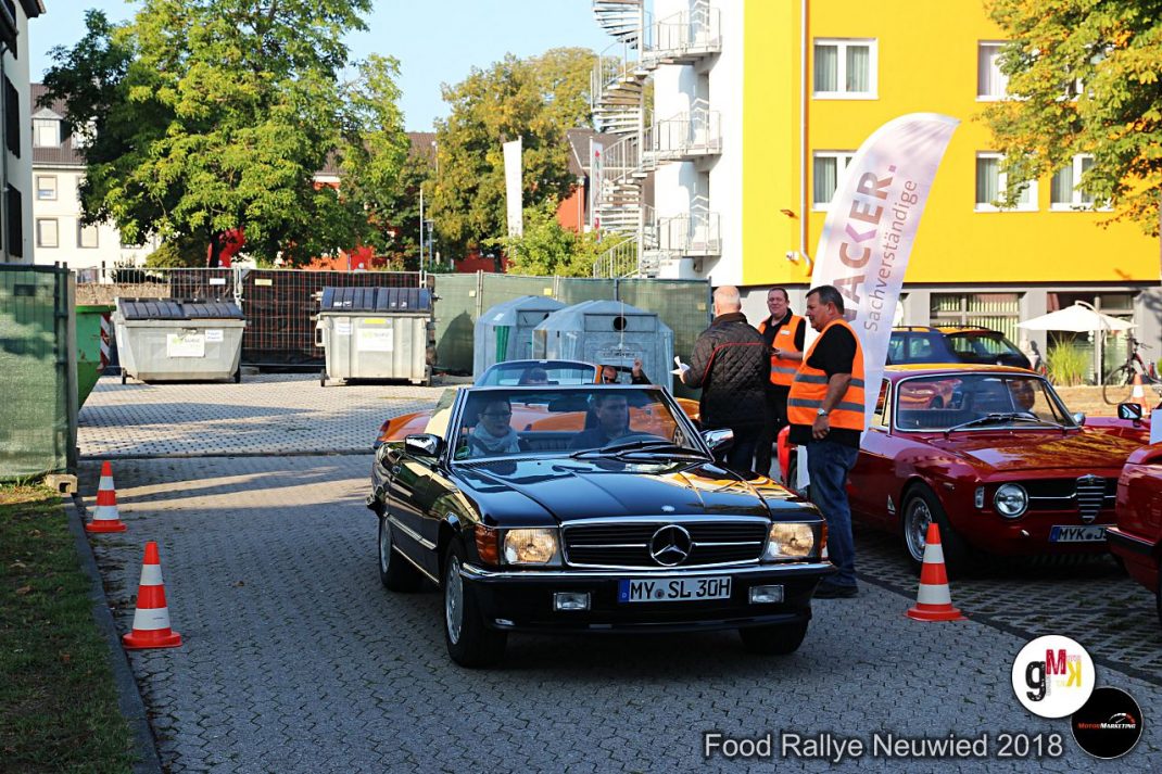 Schwarzer Mercedes-Benz Oldtimer-Cabrio mit orangem Interieur bei der Food Rallye Neuwied 2018, daneben rotes Youngtimer-Fahrzeug und Organisatoren in Westen