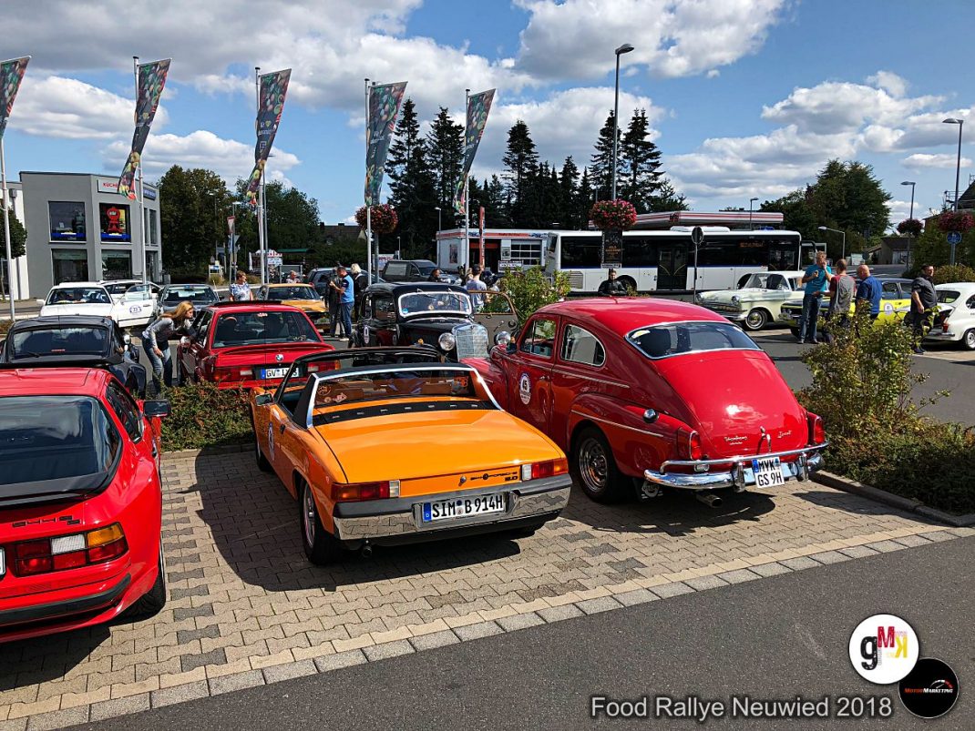 Oldtimer-Parkplatz mit roten und orangefarbenen Fahrzeugen, Besuchern und Flaggen bei der Food Rallye Neuwied