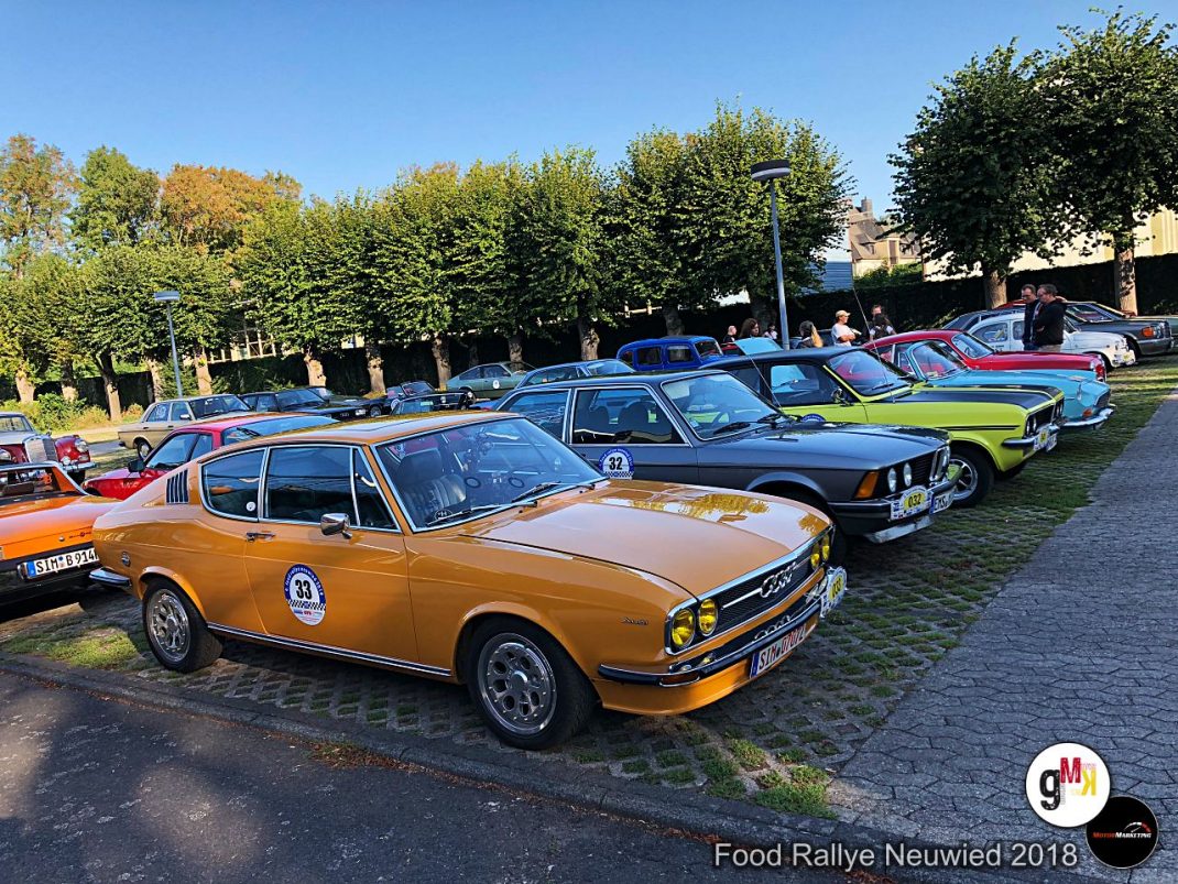 Oldtimer-Fahrzeuge in Pastelltönen stehen zur Food Rallye Neuwied 2018 auf einem gepflasterten Platz mit Bäumen im Hintergrund