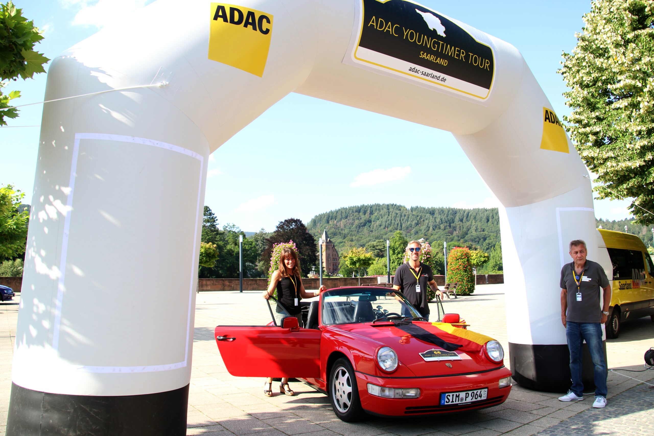 Roter Youngtimer-Sportwagen mit Teilnehmern und Betreuern unter dem Zielportal der ADAC Youngtimer Tour Saarland