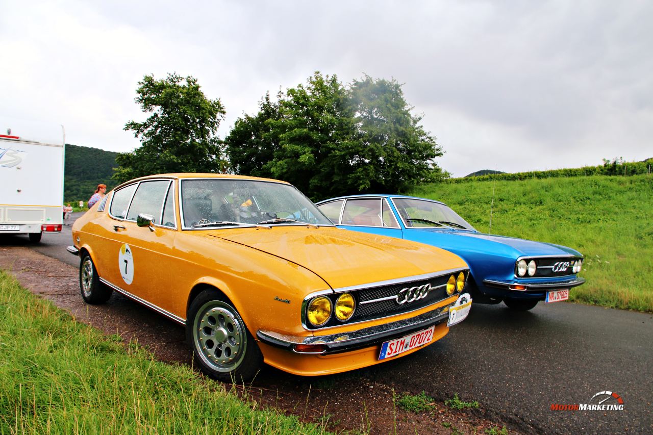 Zwei Oldtimer-Limousinen nebeneinander auf einer Straße bei der Rhein-Hunsrück-Classic, ein orange-goldener und ein blauer Wagen mit Rallyenummern