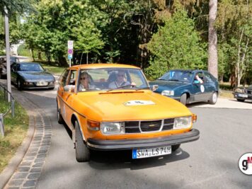 Orangefarbener Saab-Youngtimer mit Startnummer fährt voraus, begleitet von weiteren Oldtimern auf Waldstraße zur ADAC Oldtimerfahrt