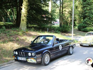 Schwarzes Oldtimer-Cabrio mit Startnummer an der ADAC Oldtimerfahrt Hessen-Thüringen, im Hintergrund weitere Teilnehmerfahrzeuge unter Bäumen