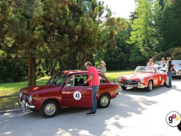 Bordeauxrote Oldtimer-Coupés mit Startnummern in einer Reihe auf sonniger Parkplatzallee, Teilnehmer bei der ADAC Oldtimerfahrt