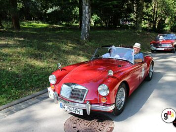 MG-Roadster in Rot mit Fahrer bei der ADAC Oldtimerfahrt Hessen-Thüringen, im Hintergrund weitere Oldtimer-Cabrios unter Bäumen