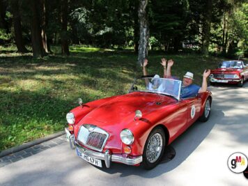 Roter Oldtimer-Sportwagen mit winkendem Fahrer auf Parkplatz während der ADAC Oldtimerfahrt Hessen-Thüringen, weitere Fahrzeuge im Hintergrund