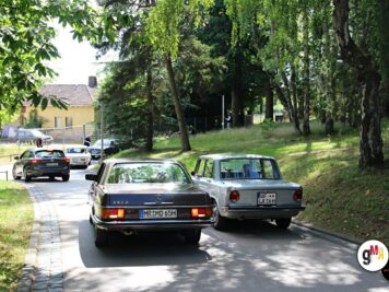 Zwei Oldtimer-Limousinen fahren auf einer Parkplatzstraße unter hohen Bäumen während der ADAC Oldtimerfahrt Hessen-Thüringen