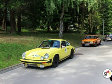 Gelber Porsche 911 und orange Limousine fahren hintereinander auf einer Straße unter Bäumen bei der ADAC Oldtimerfahrt Hessen-Thüringen
