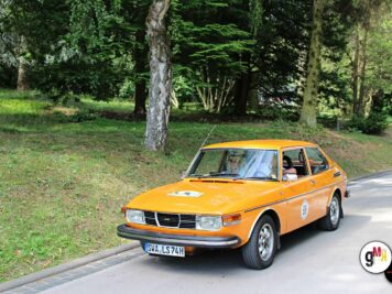 Orangefarbener Saab-Youngtimer mit zwei Insassen auf Parkplatz zwischen Bäumen während der ADAC Oldtimerfahrt Hessen-Thüringen