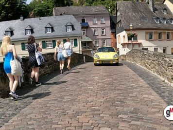 Gelber Porsche 911 fährt durch malerische Altstadt-Gasse, Zuschauer beobachten die Oldtimer-Rallye von der Seite