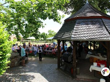 Teilnehmer und Besucher der ADAC Oldtimerfahrt unter einem großen Pavillon auf einem Parkplatz mit Grünflächen
