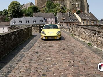 Gelber Oldtimer-Sportwagen auf gepflasterter Straße vor mittelalterlicher Burg mit Fachwerk- und Steinbauten