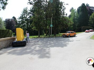 Oldtimer-Cabrio in Orange auf Parkplatz mit Baumkulisse, Teilnehmer und Hindernisstrecke bei ADAC-Oldtimerfahrt