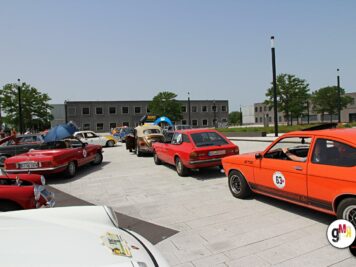 Oldtimer-Fahrzeuge verschiedener Epochen stehen auf einem Platz zur ADAC Oldtimerfahrt Hessen-Thüringen, darunter rote und orange Sportwagen sowie Limousinen