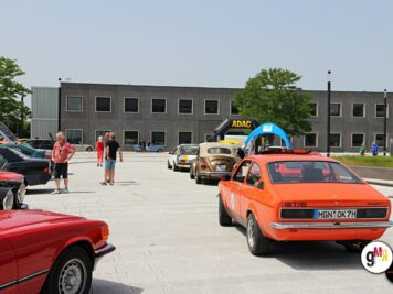 Oldtimer-Rallye auf großem Platz mit Opel-Limousine im Vordergrund, roten Klassikern und Besuchern bei der ADAC Oldtimerfahrt Hessen-Thüringen