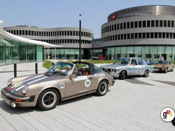 Oldtimer-Sportwagen mit Startnummer stehen auf großem Platz vor moderner Architektur während der ADAC Oldtimerfahrt