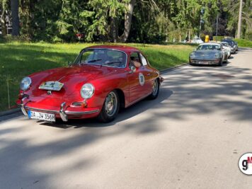 Roter Porsche 356 Coupé führt Oldtimer-Kolonne auf von Bäumen gesäumter Straße bei ADAC-Fahrt an