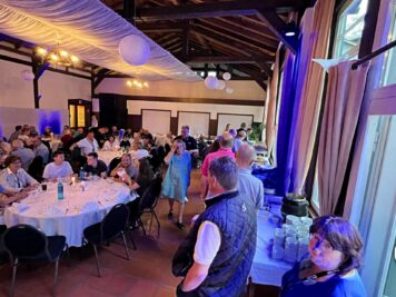 Veranstaltungssaal mit runden Tischen, an denen Teilnehmer der ADAC Oldtimerfahrt Hessen-Thüringen beim Abendessen zusammenkommen, blauviolette Beleuchtung