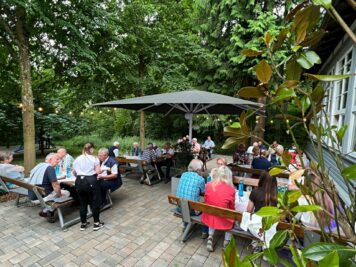 Teilnehmer der ADAC Oldtimerfahrt Hessen-Thüringen sitzen in Grüppchn an Picknickbänken unter Schirm und Bäumen