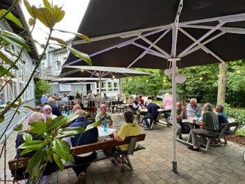 Teilnehmer der ADAC Oldtimerfahrt Hessen-Thüringen sitzen unter Sonnenschirmen auf einer Terrasse beim Pausenstopp