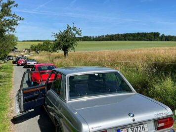 Silberner Oldtimer-Limousine mit offener Tür auf Landstraße, dahinter weitere Fahrzeuge der ADAC Oldtimerfahrt Hessen-Thüringen in Feldlandschaft