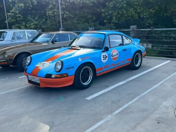 Porsche 911 in Gulf-Lackierung mit Rennnummern neben weiteren Oldtimern auf Parkplatz bei der ADAC Oldtimerfahrt Hessen-Thüringen