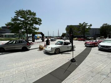 Oldtimer und Youngtimer parken auf einem Platz mit Absperrgitter, im Hintergrund Gebäude und Bäume bei der ADAC Oldtimerfahrt Hessen-Thüringen