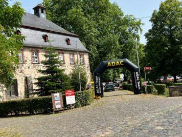 Oldtimer-Rallye Startbereich vor historischem Steingebäude mit ADAC-Zieltor und parkenden Fahrzeugen
