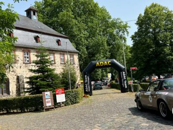 Oldtimer-Sportcoupe fährt unter schwarzem ADAC-Bogen bei der Oldtimerfahrt Hessen-Thüringen vor historischem Steingebäude
