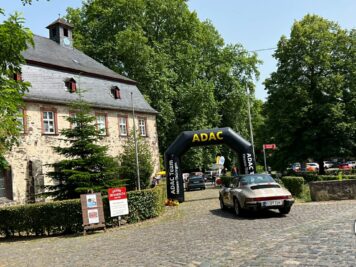 Oldtimer-Sportwagen fährt unter ADAC-Starterportal an historischem Schloss vorbei zur Oldtimerfahrt Hessen-Thüringen