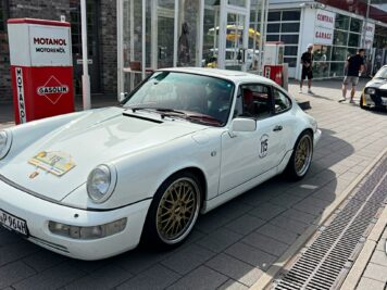 Weißer Porsche 911 Carrera mit Startnummer auf Platz beim ADAC Oldtimer-Event, Tankstelle im Hintergrund