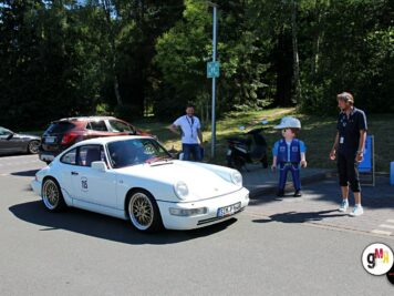 Weißer Oldtimer-Sportwagen mit Startnummer an einer Kontrollstelle der ADAC Oldtimerfahrt, Organisatoren und Teilnehmer im Hintergrund