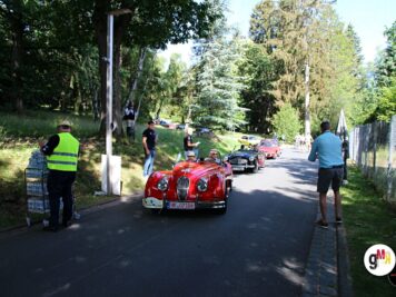 Roter Oldtimer-Roadster fährt auf bewaldeter Strecke während der ADAC Oldtimerfahrt Hessen-Thüringen, Helfer in Warnwesten betreuen die Route