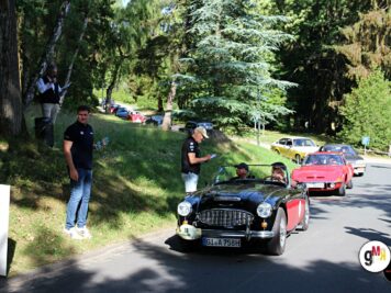 Oldtimer-Roadster und weitere klassische Fahrzeuge fahren durch grüne Waldlandschaft bei der ADAC Oldtimerfahrt Hessen-Thüringen, Betreuer stehen am Straßenrand