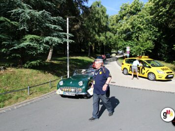 Teilnehmer der ADAC Oldtimerfahrt Hessen-Thüringen vor einem grünen Oldtimer-Sportwagen und gelben Begleitfahrzeugen in parkähnlicher Umgebung