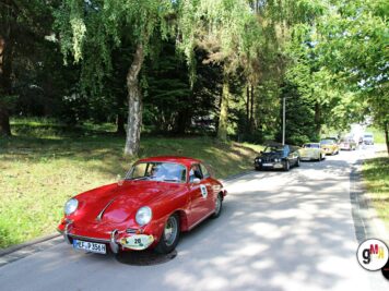 Roter Porsche 356 Coupé mit Startnummer führt Oldtimer-Kolonne durch parkähnliche Landschaft bei ADAC-Rallye