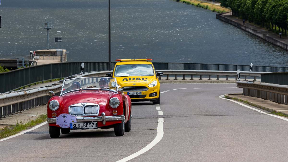 Roter MG-Sportwagen und gelbes ADAC-Begleitfahrzeug auf Brücke über Wasser während Oldtimer-Tour