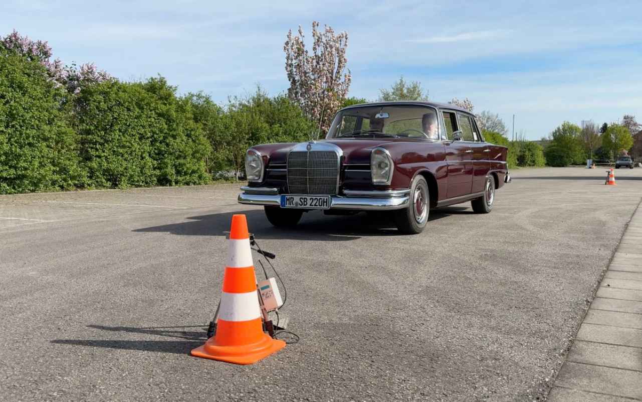 Bordeauxroter Oldtimer-Limousine beim Lichtschrankenfahren-Training auf Parkplatz mit Verkehrskegeln