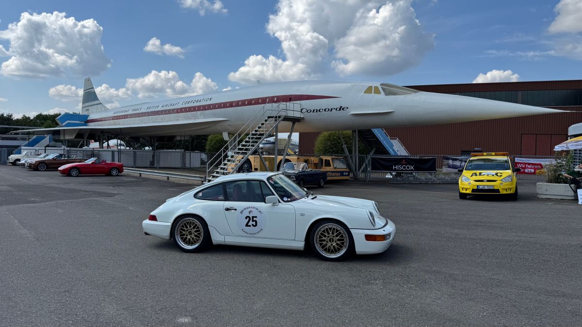 Youngtimer-Sportwagen mit Rallye-Startnummer vor Concorde-Überschallflugzeug auf Ausstellungsgelände