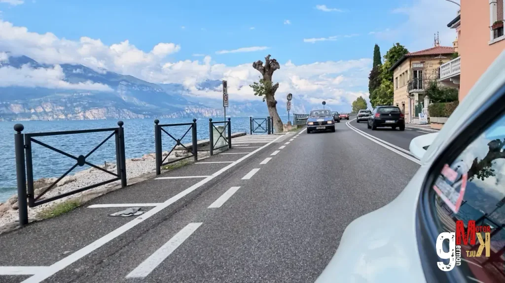 Oldtimer-Cabrio auf Küstenstraße am Gardasee mit Bergblick und mediterraner Architektur