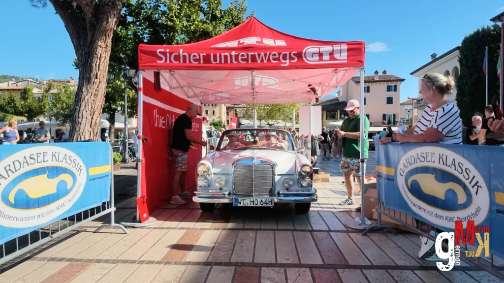 Oldtimer-Limousine durchfährt Zielbereich der ADAC Gardasee Klassik unter rotem Werbebogen auf italienischem Marktplatz