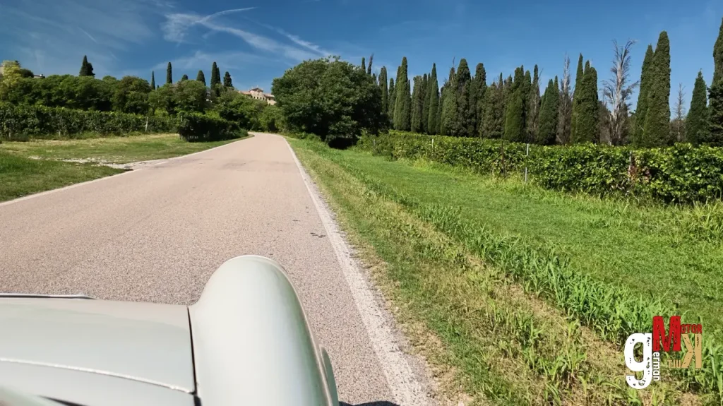 Blick aus einem Oldtimer-Cabrio auf eine kurvenreiche Landstraße mit Zypressen und Grünflächen beim Klassik-Event am Gardasee
