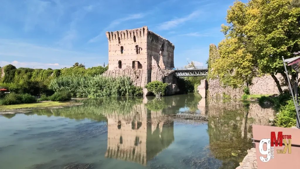 Historischer Wehrturm an einem Fluss mit Brücke, umgeben von grüner Vegetation am Gardasee, Schauplatz der ADAC Gardasee Klassik